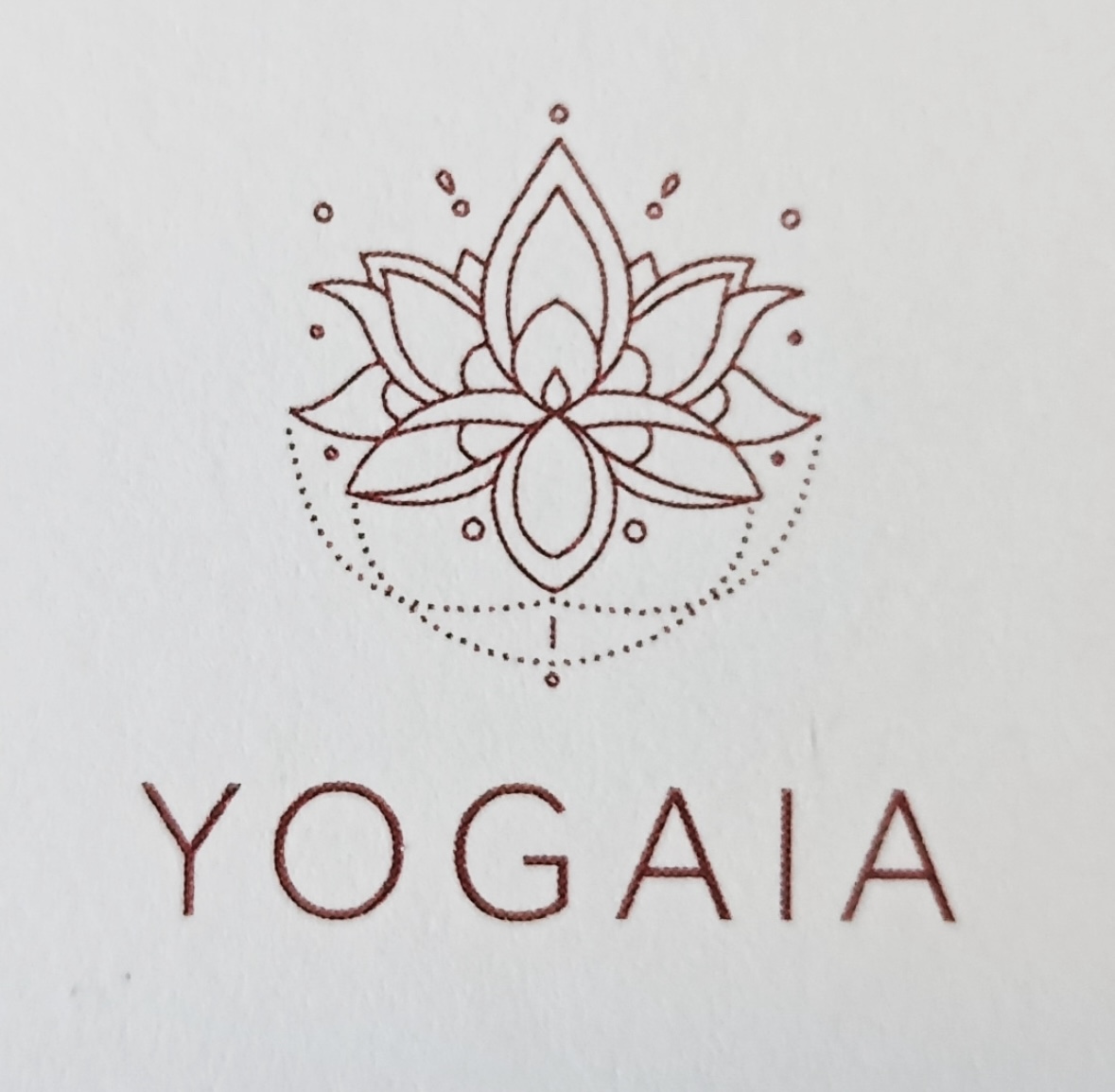 Bild von einer weinroten Lotusblume mit der Unterschrift YOGAIA auf einem grauen Hintergrund.